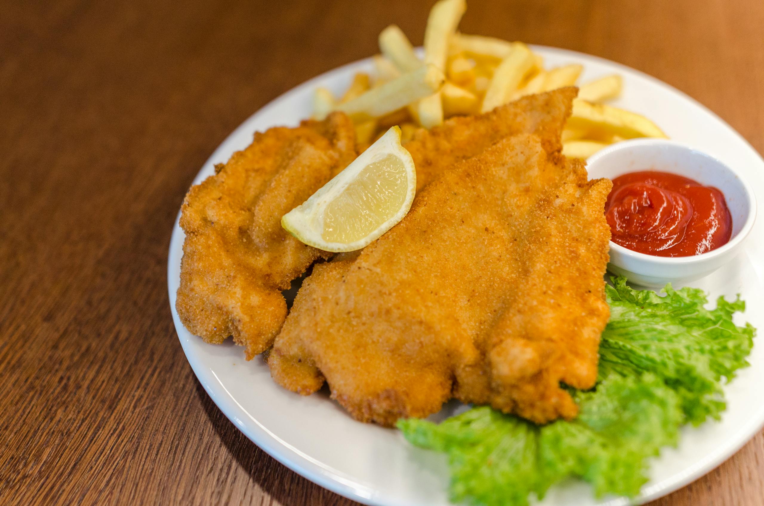 Delicious schnitzel served with fries, lettuce, lemon, and ketchup on a wooden table.