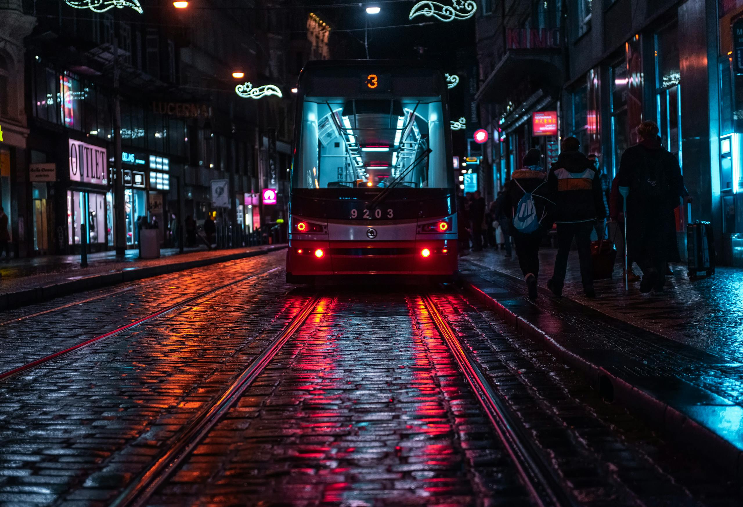 Tram on a cobblestone street in Prague, reflecting city lights on a rainy evening.