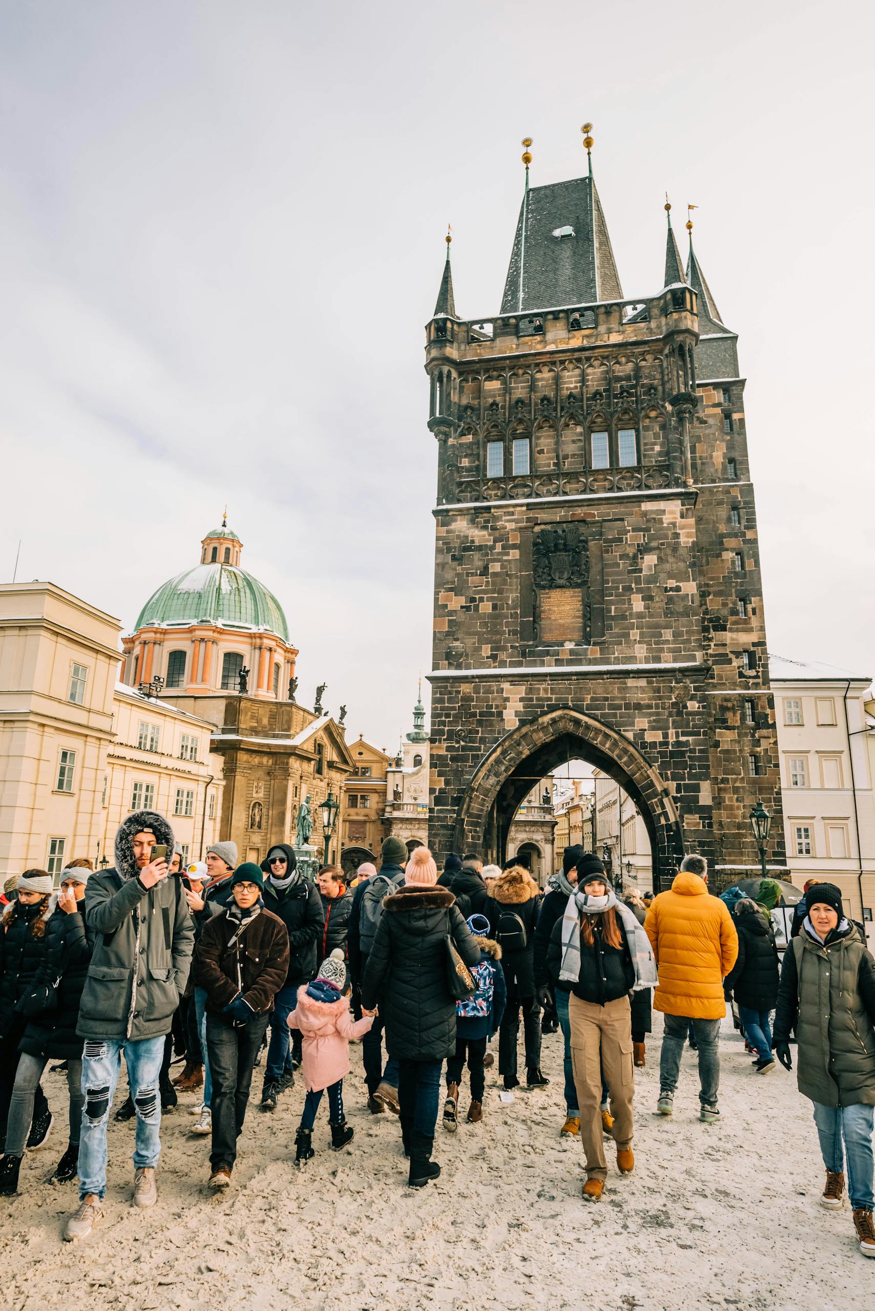 A busy winter day with tourists at the Old Town Bridge Tower in Prague, showcasing historic architecture and seasonal attire.