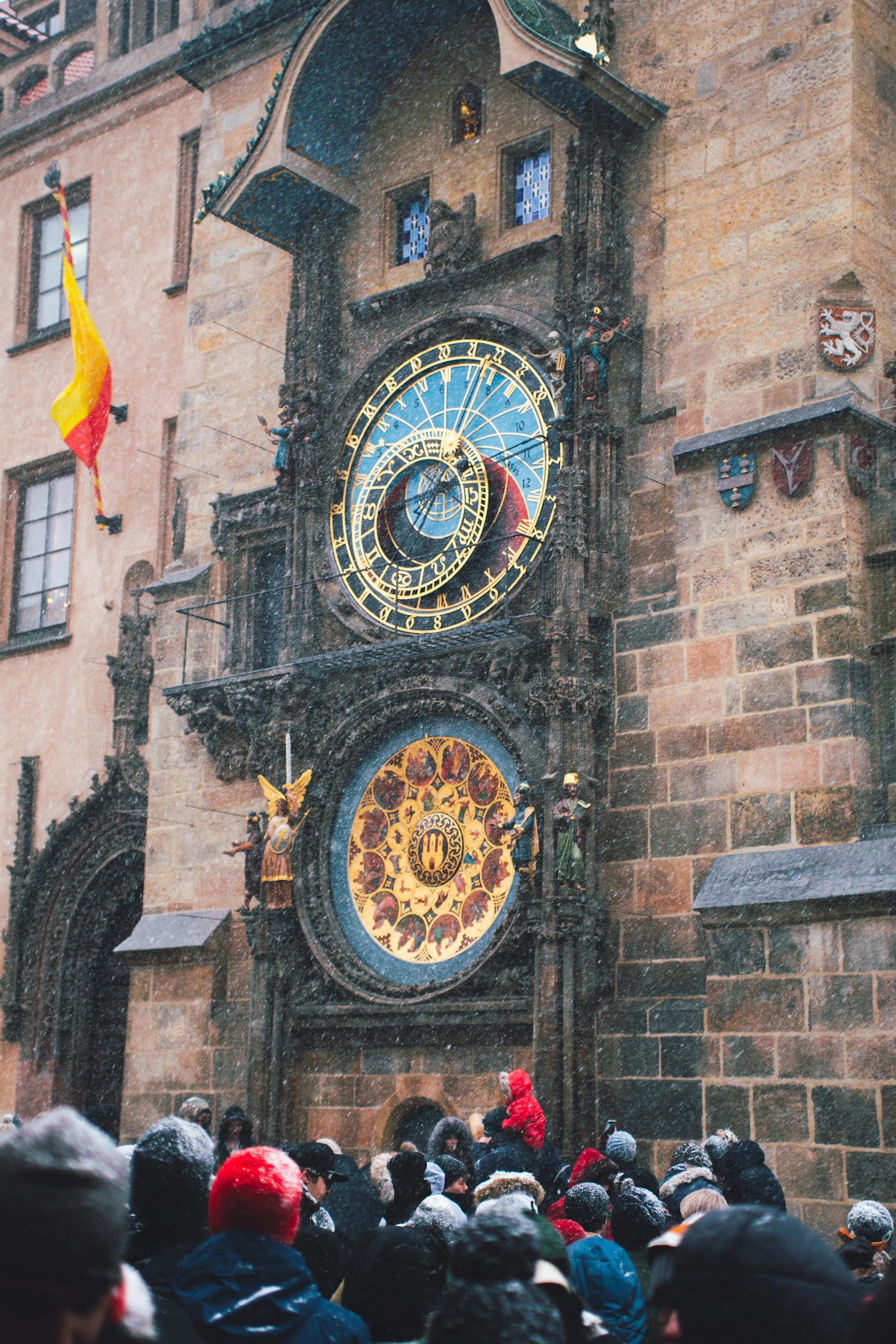 A winter crowd gathers near the historic Prague Astronomical Clock in the snow.